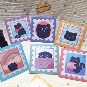 May include: A collection of square stickers featuring cartoon cat illustrations in a postage stamp design. Each sticker has a different cat design, with pastel colors and numbers in the corners. The stickers are arranged on a textured surface.