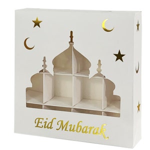 May include: White cardboard gift box with a cut-out design of a mosque. The box has gold foil accents of stars, crescents, and the words "Eid Mubarak".