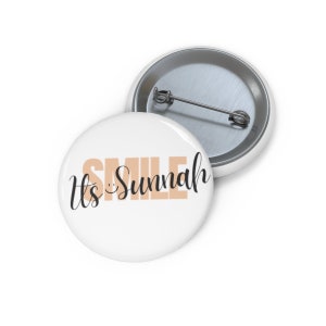 May include: White button with a peach colored graphic that says "It's Sunnah" with a smiley face in the word "smile".