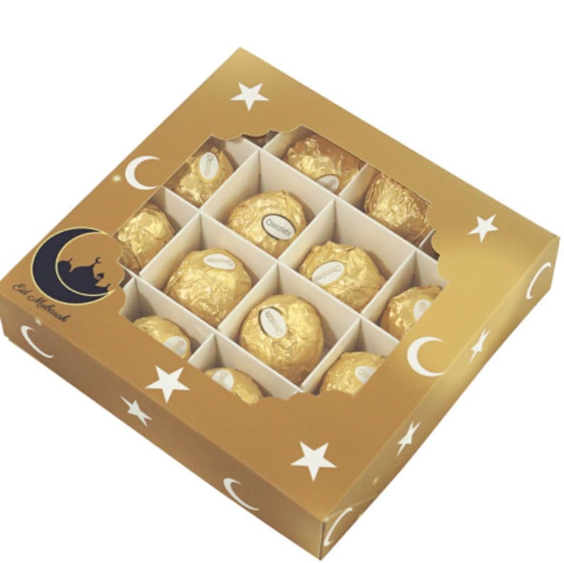 May include: A gold box with a clear window, decorated with stars and crescent moons, containing 12 individually wrapped chocolates. The box says "Eid Mubarak" on the front.