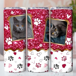 May include: A set of three stainless steel tumblers with a pink glitter background and paw print designs. Each tumbler features a photo of a grey cat with a white chest.