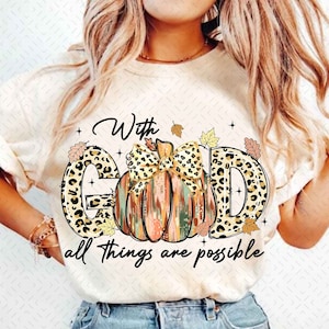 May include: White t-shirt with a graphic of a pumpkin with a bow and the words "With God all things are possible". The pumpkin is decorated with a leopard print pattern and fall leaves.