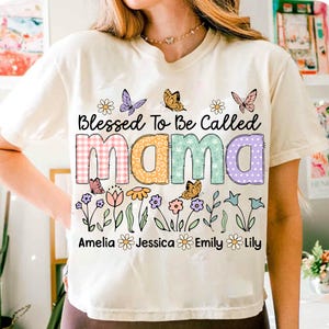 Puede incluir: Camiseta blanca con un gr&aacute;fico colorido que dice "Blessed To Be Called Mama" con mariposas y flores. Los nombres Amelia, Jessica, Emily y Lily est&aacute;n impresos debajo del gr&aacute;fico.