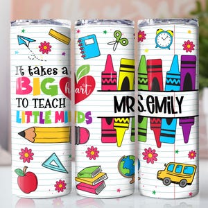 May include: A white tumbler with a school-themed design. It features colorful illustrations of school supplies, including crayons, a pencil, and a school bus. The text reads "It takes a BIG heart to teach LITTLE MINDS" and "MRS. EMILY".