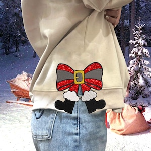 May include: A beige sweatshirt with a red and gray glitter bow and black boots embroidered on the back. The boots have white fur trim.