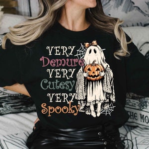 May include: Black t-shirt with a graphic of a ghost holding a pumpkin. The text "Very Demure Very Cutesy Very Spooky" is printed on the shirt.