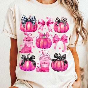 May include: A white t-shirt with a pink and black fall-themed design. The design features pumpkins, bows, and a fall-themed drink.