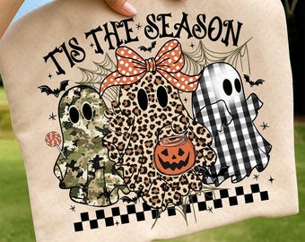 May include: A beige Halloween-themed design featuring three cartoon ghosts. One ghost has a camouflage pattern, another has a leopard print, and the third is checkered. The text "TIS THE SEASON" is above the ghosts. A bow and a jack-o'-lantern are also present.
