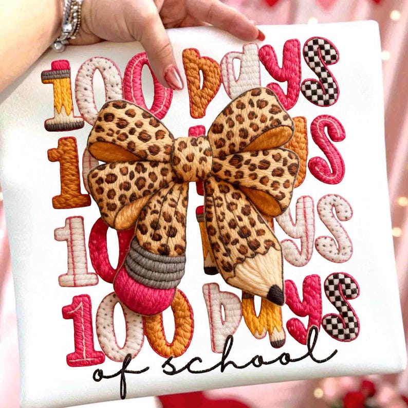 Pode incluir: Tecido branco com texto bordado e um grande la&ccedil;o. O texto diz "100 Days of School" em v&aacute;rias cores. O la&ccedil;o tem um design de estampa de leopardo e um l&aacute;pis &eacute; incorporado no design.