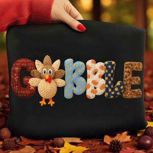 May include: Black pillow with the word "GOBBLE" in colorful, textured letters. The "G" is red, the "O" features a turkey, the "B" is blue, the second "B" is white with orange pumpkins, and the "LE" is brown.