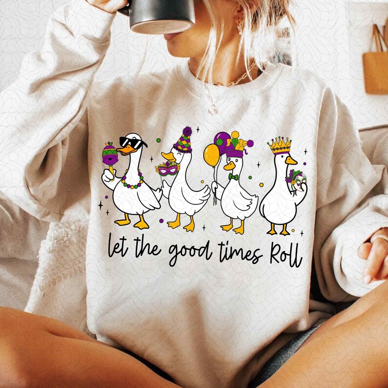 May include: Cream-colored sweatshirt featuring a graphic of four white ducks dressed for a celebration. Each duck is wearing festive accessories like sunglasses, hats, and crowns, holding items like a lollipop and balloons. The phrase "Let the good times Roll" is written below.