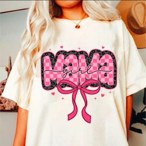 May include: White t-shirt with a pink and black graphic that says "Mama girl" with a pink bow.