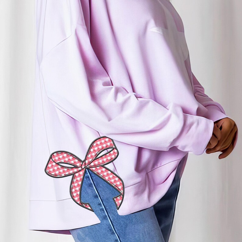Puede incluir: Una sudadera de manga larga lavanda con un lazo de vichy rosa y blanco en la costura lateral.
