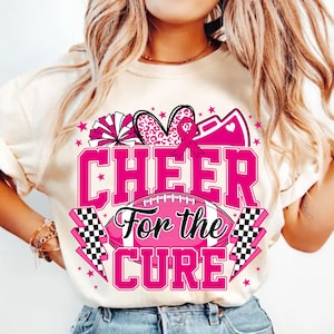 May include: White t-shirt with a pink graphic design that says "Cheer For the Cure". The graphic includes a pink ribbon, a heart with leopard print, a cheerleader's pom-pom, and a football.