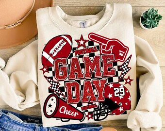 May include: A beige sweatshirt with a red and black graphic design that says "Football Game Day" with a football, a megaphone, a helmet, and a hand pointing.