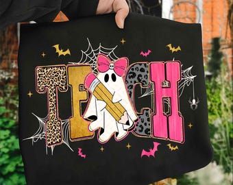 Może przedstawiać: Czarna torba z napisem "TEACH" w halloweenowym designie. Litery mają wzory w panterkę, złote i różowe akcenty. Duch trzymający ołówek znajduje się na środku, z nietoperzami, pająkami i pajęczynami.