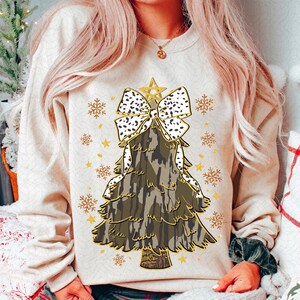 Può includere: Una felpa color crema con un design di albero di Natale mimetico. L'albero è sormontato da un fiocco a pois bianchi e neri e da una stella dorata.