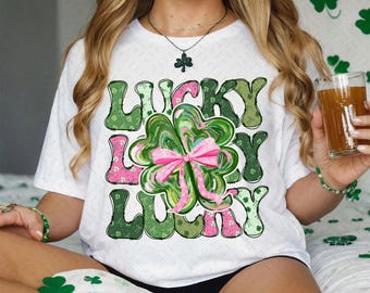 May include: White t-shirt with a green and pink shamrock design and the text "Lucky Lucky" in a retro font.