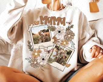 Puede incluir: Sudadera beige con la palabra "Mama" en letras marrones. El diseño incluye elementos florales, mariposas y dos fotos estilo polaroid. Las fotos parecen mostrar a una familia. La sudadera tiene cuello redondo.
