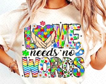 May include: White t-shirt with a colorful graphic design featuring a puzzle piece heart, the word "LOVE" and the text "needs no WORDS".