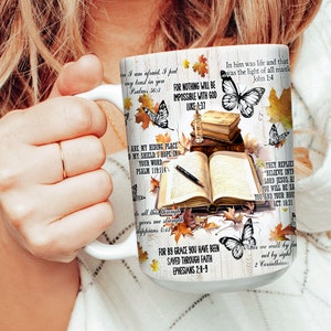 May include: White ceramic mug with a colorful design featuring butterflies, leaves, and bible verses. The mug has a handle and is filled with a brown liquid. The text on the mug includes verses from the Bible, such as "For nothing will be impossible with God" and "In him was life and that was the light of all mankind."