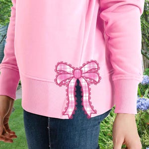 May include: Pink sweatshirt with a large pink and white plaid bow with lace trim on the back.