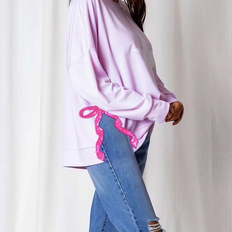 Puede incluir: Una sudadera de manga larga lavanda con un detalle de cinta rosa en el lateral.