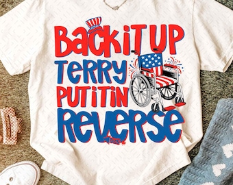 May include: Cream-colored t-shirt with the text "Back it UP Terry Putin in Reverse" in red and blue. The design includes a wheelchair decorated with the American flag and a patriotic hat.
