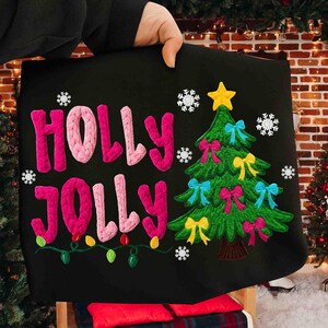 Könnte beinhalten: Schwarzes Kissen zum Thema Weihnachten mit den Worten "HOLLY JOLLY" in rosa, gestrickten Buchstaben. Auf der rechten Seite befindet sich ein grüner Weihnachtsbaum mit bunten Schleifen und einem gelben Stern. Schneeflocken und Lichterketten ergänzen das Design.