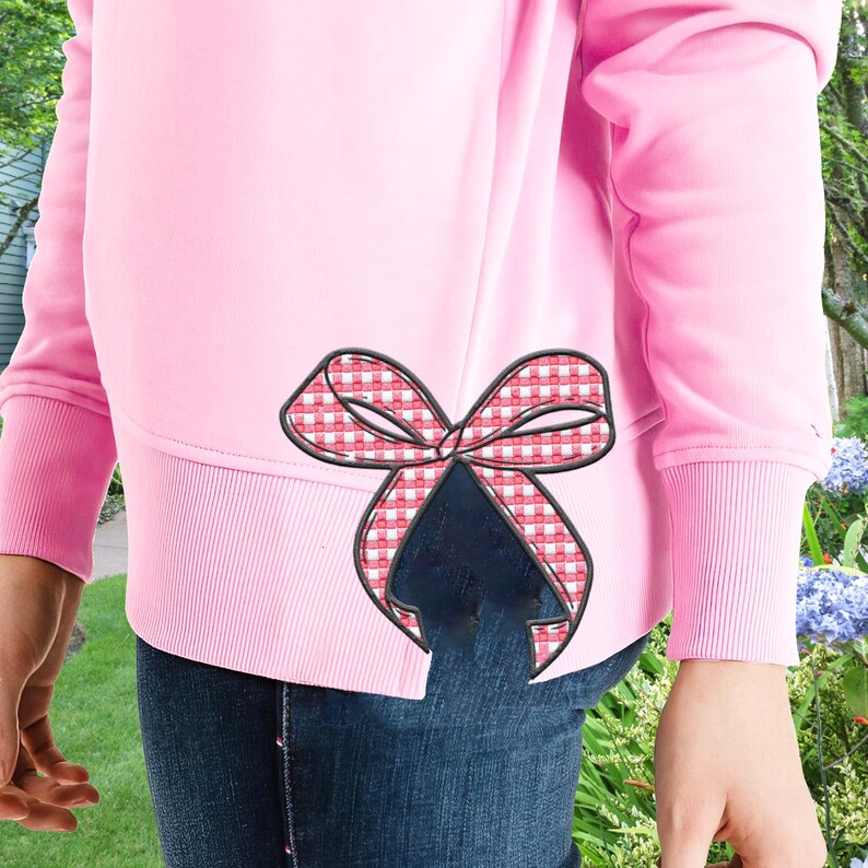 Puede incluir: Una sudadera rosa con un lazo de cuadros rojos y blancos en el lateral. La sudadera tiene una abertura lateral y un dobladillo de canal&eacute;.