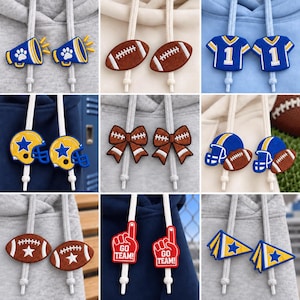 Op de afbeelding: Een collectie van negen paar decoratieve trekkoordbedels voor hoodies met diverse sportthema-ontwerpen, waaronder megafoons, footballs, shirts met het nummer één, helmen, strikken, schuimvingers met de tekst GO TEAM en wimpels.