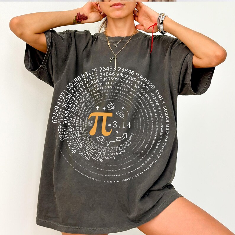 May include: A dark gray oversized t-shirt with a white graphic print of a spiral of numbers and the mathematical symbol pi. The graphic also includes the equation "&pi; = 3.14" and other mathematical symbols.