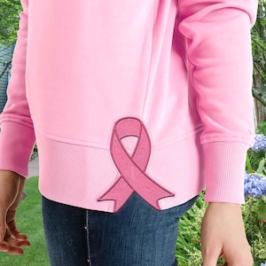 Op de afbeelding: Roze trui met een geborduurd roze lint aan de zijkant. De trui heeft lange mouwen en een geribbelde zoom.