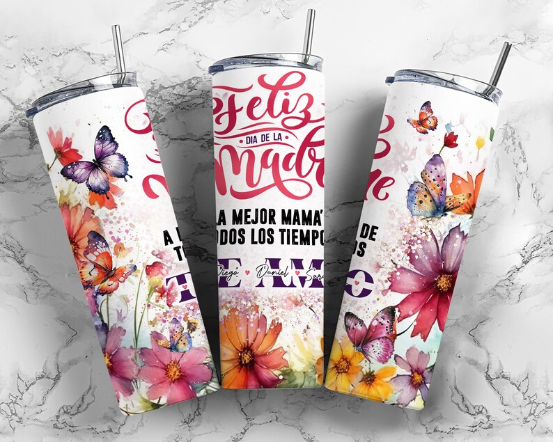 May include: A white stainless steel tumbler with a watercolor design of butterflies and flowers. The text "Feliz Dia de la Madre" and "A la mejor mama de todos los tiempos te amo" is printed on the tumbler.