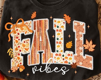 May include: Black sweatshirt with the words "FALL vibes" in a fall-themed design. The letters are decorated with autumn leaves, pumpkins, and floral patterns. An orange bow is on the letter "F".