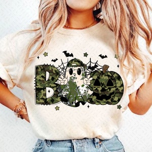 May include: A white t-shirt with a green camouflage print of a ghost, pumpkin, and the word "BOO".