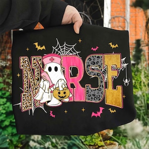 May include: Black tote bag with a Halloween-themed design. The word "NURSE" is displayed with leopard print, pink, and gold lettering. A ghost in a nurse's hat holds a syringe and a jack-o'-lantern. Bats, spiderwebs, and stars complete the design.