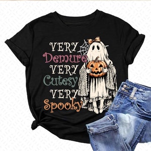 May include: Black t-shirt with a white ghost holding a jack-o'-lantern. The text "Very Demure Very Cutesy Very Spooky" is printed on the shirt.
