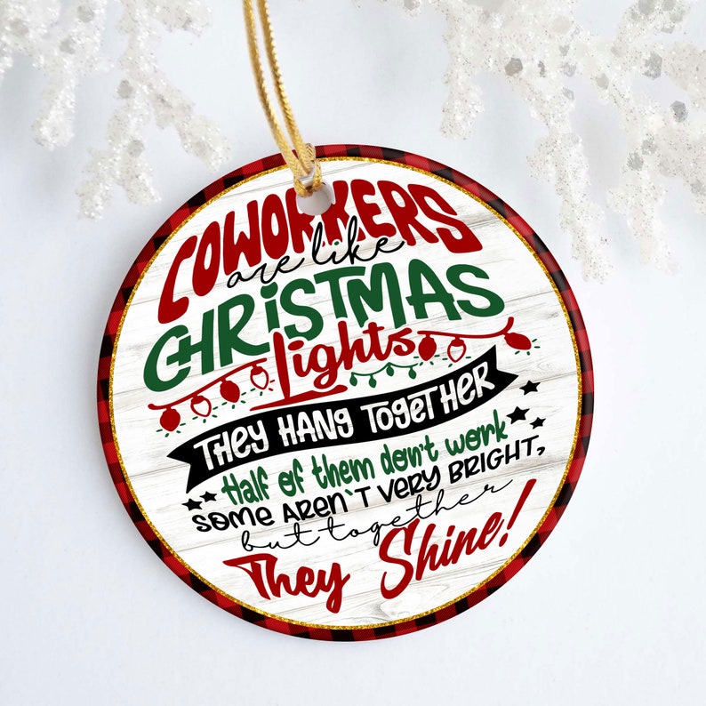 May include: Round Christmas ornament with a white woodgrain background and red and black buffalo plaid trim. The ornament features the text "Coworkers are like Christmas lights. They hang together. Half of them don't work, some aren't very bright, but together they shine!"