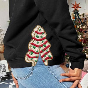 May include: Black sweatshirt with a gingerbread Christmas tree design. The gingerbread tree has red and green accents. The sweatshirt is made of a soft material and is perfect for the holiday season.