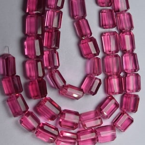 Puede incluir: Una hebra de cuentas de vidrio facetadas de color rosa. Las cuentas son de forma rectangular y tienen una apariencia translúcida.