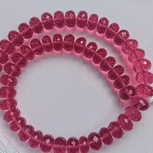 Puede incluir: Una hebra de cuentas de cristal facetadas de color rosa con borlas blancas en cada extremo.