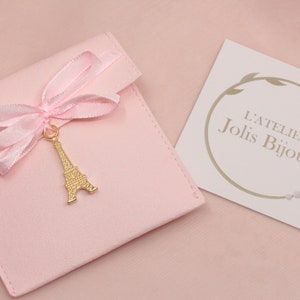 May include: A pink velvet jewelry pouch with a gold Eiffel Tower charm and a pink satin ribbon. The pouch has a white card with the text "L'Atelier Jolis Bijoux".
