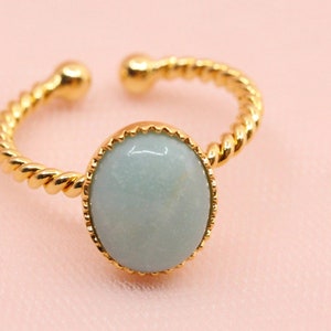 May include: A gold ring with a twisted band and a light blue oval-shaped gemstone set in a gold bezel.