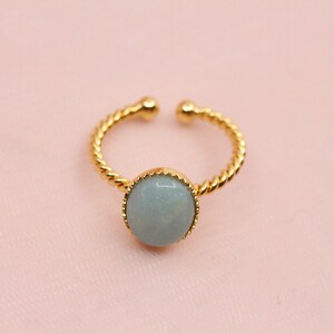 May include: A gold ring with a twisted band and a light blue gemstone set in a gold bezel.