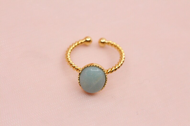 May include: A gold ring with a twisted band and a light blue gemstone set in a gold bezel.