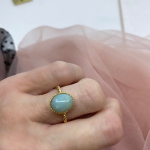 May include: A gold ring with a light blue oval gemstone set in a twisted band.
