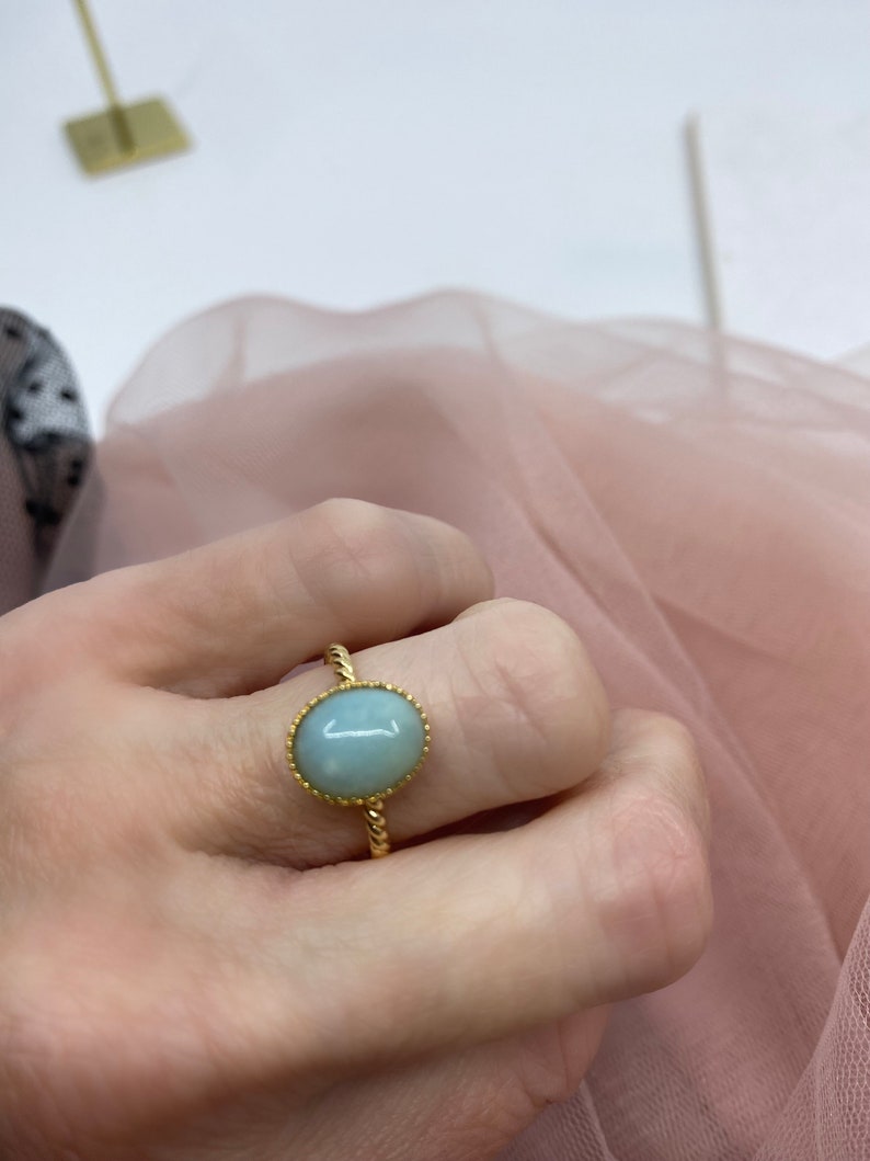 May include: A gold ring with a light blue oval gemstone set in a twisted band.