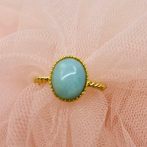 May include: A gold ring with a light blue oval gemstone set in a gold bezel. The ring has a twisted band.