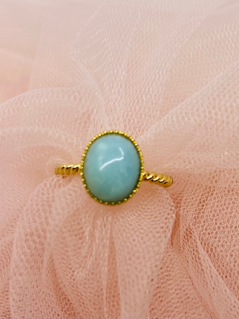 May include: A gold ring with a light blue oval gemstone set in a gold bezel. The ring has a twisted band.